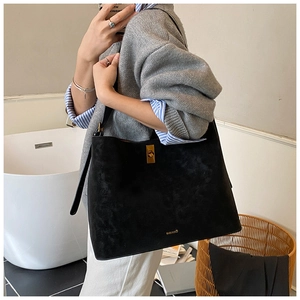 Detail of black suede tote bag featuring a golden twist lock and branded logo accent
