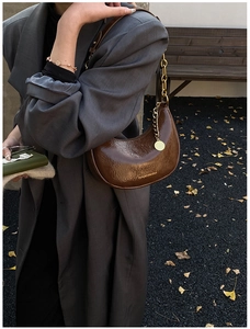 Detail of a dark brown hobo bag featuring glossy wrinkled texture and gold chain strap