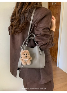 Detail of grey pebbled leather bucket bag with plush puppy charm on a brown suit