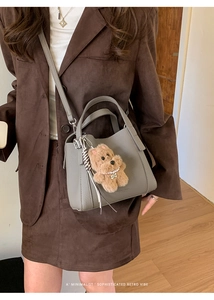 Close-up of gray pebble leather bucket bag with a cute plush dog charm and woven tassel