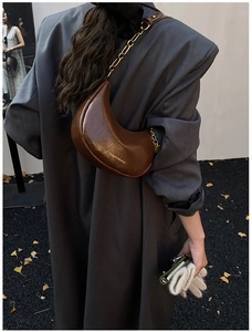 Close-up of a brown crescent shoulder bag with gold chain strap on a stylish autumn model