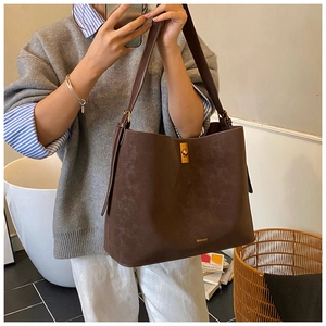Detailed close-up of dark brown suede tote bag with gold twist lock and brand logo