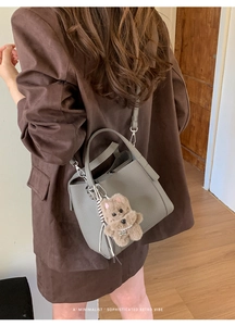 Detail of grey lychee leather bucket bag with cute brown plush bear charm and strap