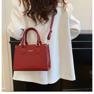 Detail of red textured leather handbag with gold hardware worn over a white suit