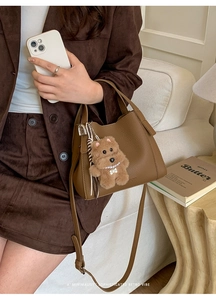 Detail of brown lychee grain leather tote with an adjustable strap and cute bear charm