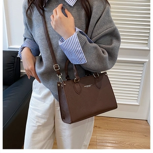 Detail view of dark brown pebble leather bag with white text and adjustable shoulder strap