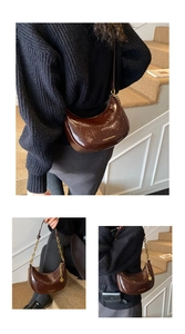 Detail of a brown patent leather half-moon bag with gold chain and sleek shoulder strap