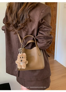 Detail of brown lychee leather bucket bag with cute plush puppy charm and pearl chain