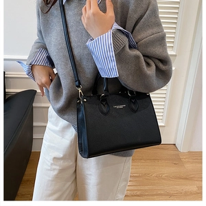 Close-up of black lychee grain leather tote bag worn by model in a modern room setting