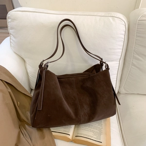 Detalle del bolso tote de ante marrón oscuro con textura mate sobre un sofá blanco