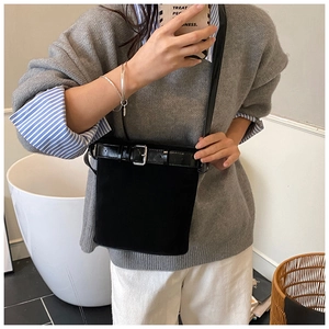 Détail d'un sac seau en daim noir avec sangle en cuir et boucle argentée dans un intérieur