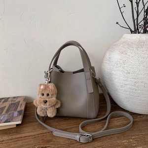 Detail of taupe leather bucket bag with teddy bear charm on a wooden surface