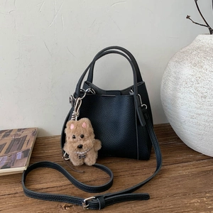 Detail of black lychee grain bucket bag with cute plush puppy charm and adjustable strap