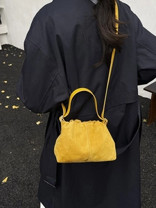 Fashionable bright yellow cloud-shaped handbag with soft texture shown on a dark coat