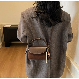 Detail of dark brown crossbody bag with beaded pendant worn by model in a grey suit
