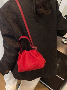 Red velvet cloud bucket bag with drawstring closure and crossbody strap on dark coat