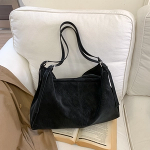 Detalle de bolso tote de ante negro con correas ajustables sobre un sofá blanco