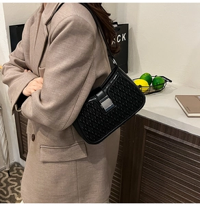 Vista laterale della borsa a tracolla intrecciata nera con fibbia su blazer marrone