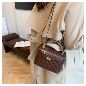 Detail of dark brown quilted chain bag with gold handle shown on a shoulder