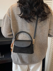 Retro black leather shoulder bag with beaded charm and adjustable strap on a gray sweater