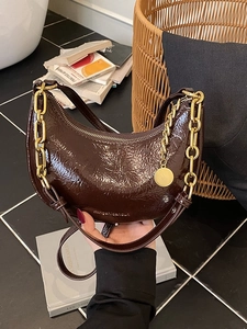 Glossy dark brown crescent handbag with gold chain detail and vintage chic design