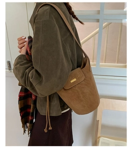 Gros plan d'un sac seau vintage marron mat avec barre dorée porté par un mannequin