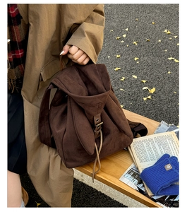 Detail of dark brown suede backpack with drawstring closure and metal buckle in autumn setting