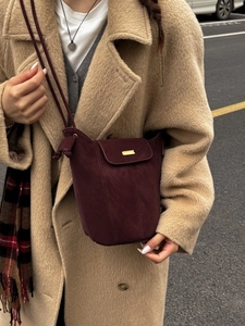 Sac seau minimaliste en daim bordeaux avec détails dorés porté par un mannequin en ville