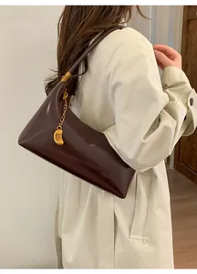 Detail view of dark brown glossy patent leather shoulder bag with gold crescent pendant