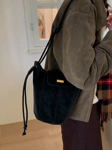 Sac seau chic en daim noir avec détails dorés porté par un mannequin dans un intérieur
