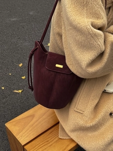 Sac seau en daim bordeaux avec fermoir doré porté par un mannequin en décor d'automne