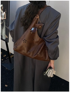 Detail of vintage brown leather hobo bag with laser-cut floral patterns and wide strap