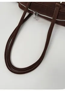 Close-up of brown suede shoulder bag with dual silver zippers and smooth handle detail