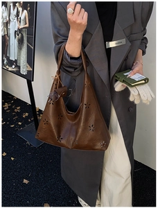 Detail of dark brown leather hobo bag with floral cutouts and hanging glasses case