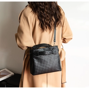 Detail of black woven leather handbag with shoulder strap on beige trench coat outfit