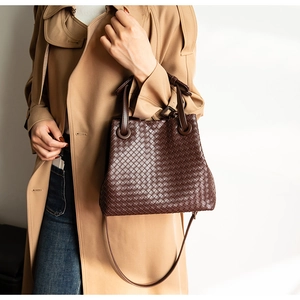 Detail of dark brown hand-woven leather tote bag worn by model with khaki trench coat