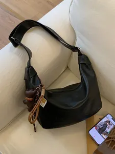 Black large capacity faux leather croissant bag with bear charm on a white sofa
