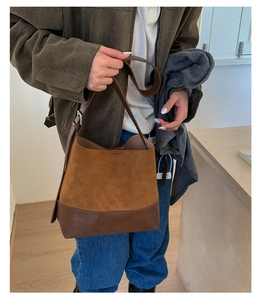 Brown leather bucket bag with mixed textures and adjustable strap shown on a model