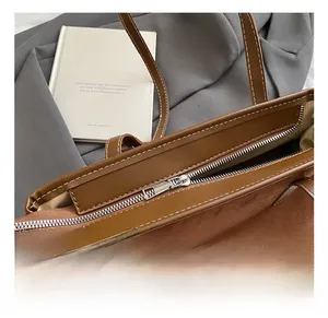 Detail of silver metal zipper and white stitching on brown suede shoulder bag