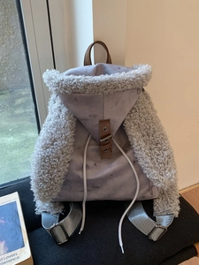 Purple suede backpack with grey faux fur trim and adjustable straps in a cozy setting