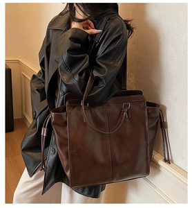Detail view of large dark brown leather tote bag with drawstrings and shoulder strap