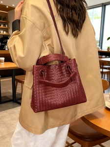 Handwoven burgundy leather handbag with top handles and shoulder strap in street style