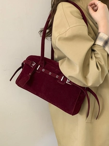 Dark red suede underarm shoulder bag with eyelet strap detail shown on a trench coat
