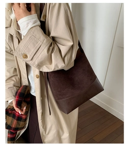 Detailed view of a dark brown suede bucket bag worn with a beige trench coat
