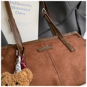 Detail of brown suede tote bag with white contrast stitching and plush bear pendant