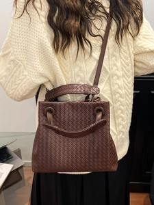Brown woven leather handbag featuring a top handle and adjustable shoulder strap