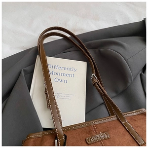 Detail of dark brown suede tote bag with contrast stitching on a grey blazer
