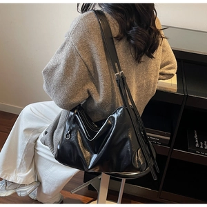 Detail of a large black glossy leather hobo bag with adjustable strap on a female model