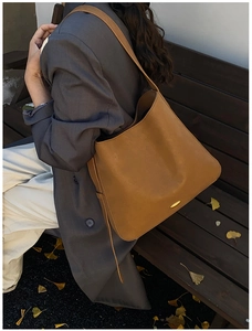Close-up of tan leather hobo bag with gold hardware detail in an autumn park setting