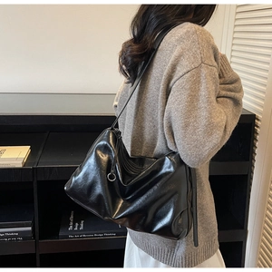 Detail of black glossy faux leather tote bag with silver ring accent on a shoulder